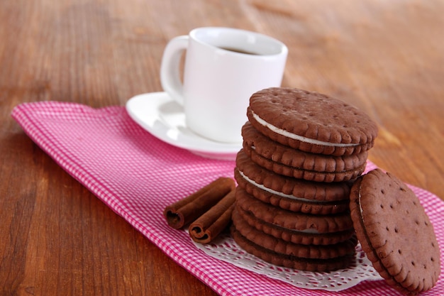 Biscoitos de chocolate com camada cremosa e xícara de café na mesa de madeira closeup