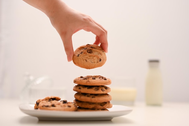 Biscoitos de chocolate recém-assados em um prato branco com uma mão feminina segurando um pedaço de biscoito