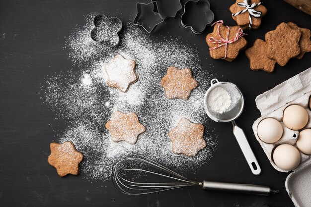 Biscoitos de gengibre assados em forma de estrela polvilhados com açúcar de confeiteiro em uma mesa preta, vista de cima