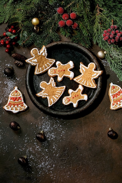 Biscoitos de gengibre caseiros tradicionais de Natal com glacê ornamentado. Homem-biscoito, anjo, sino na placa de cerâmica com decorações de Natal. Postura plana