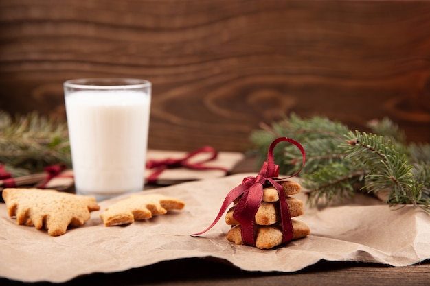 Biscoitos de gengibre de natal e um copo de leite na placa de madeira escura.