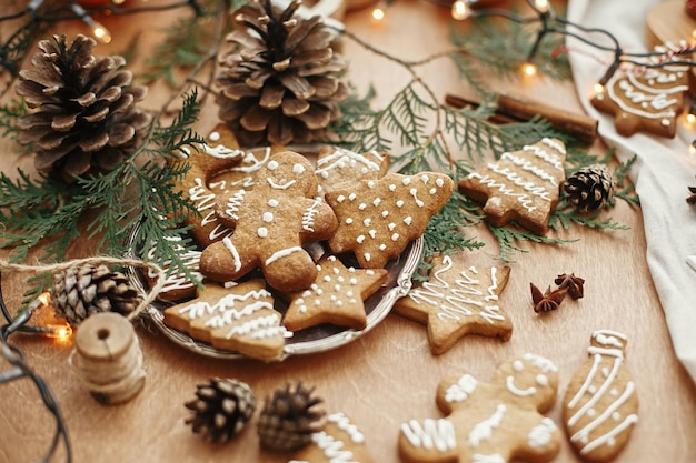 Biscoitos de gengibre de natal no prato vintage e anis canela pinhas ramos de cedro com luzes douradas na mesa rústica Biscoitos de gengibre tradicional cozido homem árvore estrela
