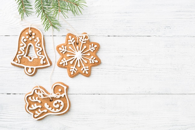 Biscoitos de gengibre de Natal pendurado no abeto vermelho sobre fundo branco de madeira, espaço de cópia.