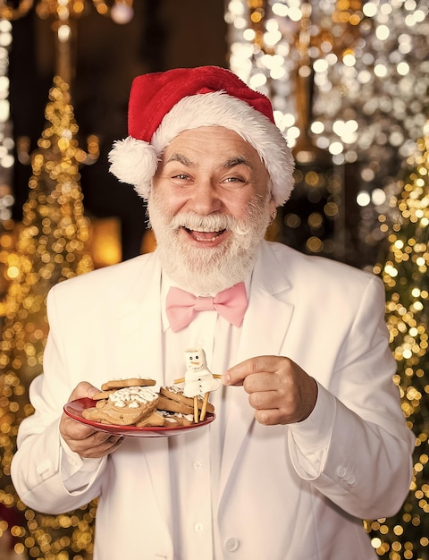 Biscoitos de gengibre feliz empresário segura biscoitos empresário sênior com chapéu de papai noel doces e guloseimas de natal decoração de natal conceito de pão de gengibre dieta café restaurante receita de culinária