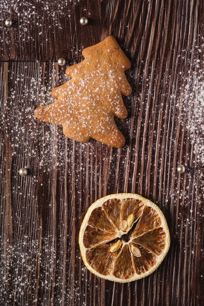 Biscoitos de gengibre na árvore de Natal, açúcar em pó na mesa de madeira, limão cítrico, vista superior