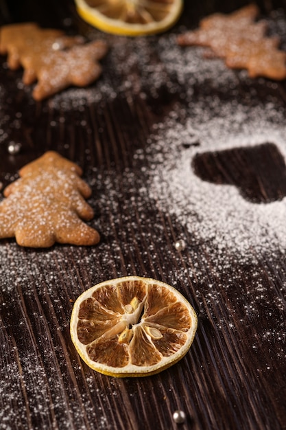 Biscoitos de gengibre no abeto de Natal, açúcar em pó na mesa de madeira, vista de ângulo, foco seletivo em limão cítrico