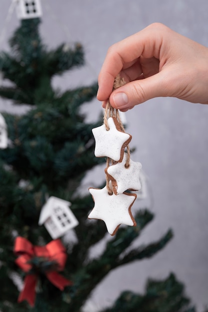 Biscoitos de gengibre para decoração de Natal. Bens de Natal assados na mão feminina. Árvore de Natal em segundo plano.