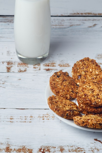 Foto biscoitos de grãos inteiros de granola saudável lanche e copo de leite na superfície de madeira.