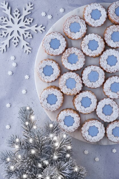 Biscoitos de Linzer de flor com glacê azul no quadro branco marmor em cima da superfície de inverno luz com árvore de Natal