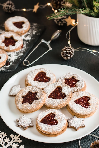 Biscoitos de Linzer prontos com geléia de baga em um prato e decorações de Natal em um fundo escuro. Cozinhar guloseimas de Natal. Estilo de vida. Visão vertical. Fechar-se