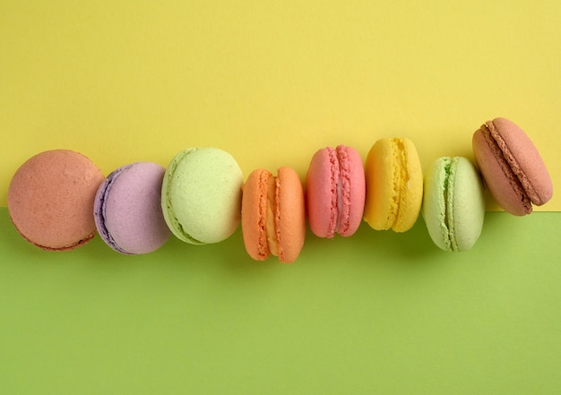 Biscoitos de macaroon multicoloridos assados em uma fileira em um verde-amarelo