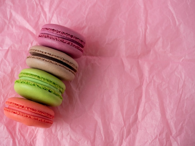 Biscoitos de macaroon tradicionais de cores diferentes mentem sobre um fundo de papel rosa. artigo isolado, doces, confeitaria. vista superior, copie o espaço.