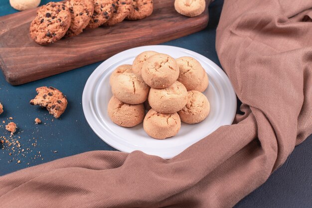 Biscoitos de manteiga em uma bandeja branca e biscoitos de aveia em uma mesa azul