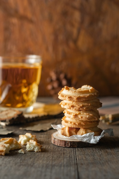 Biscoitos de manteiga empilhados e um copo de chá no fundo da mesa de madeira, foto vertical.