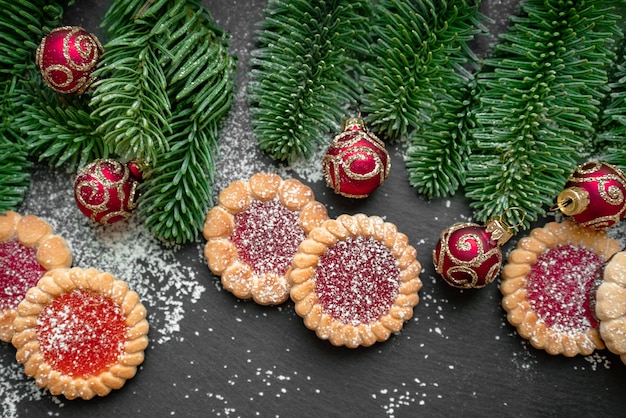 Biscoitos de mel, bolas vermelhas e ramos de abeto na superfície escura, fundo de Natal e Ano Novo