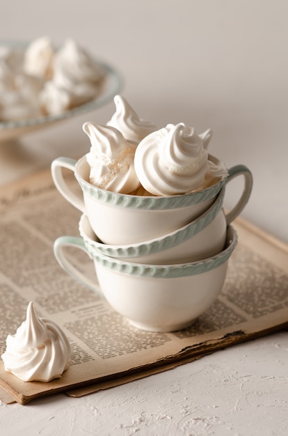 Biscoitos de merengue em xícaras de chá verde e branco em uma velha revista