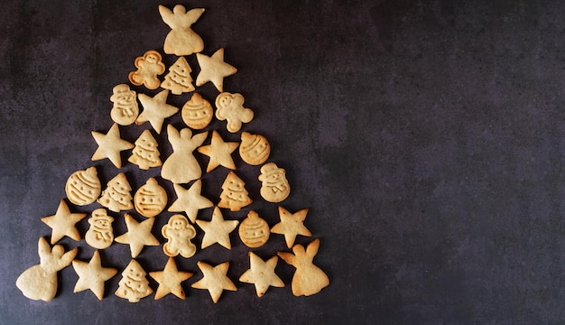 Biscoitos de natal caseiros dispostos em uma mesa escura na forma de uma árvore de natal