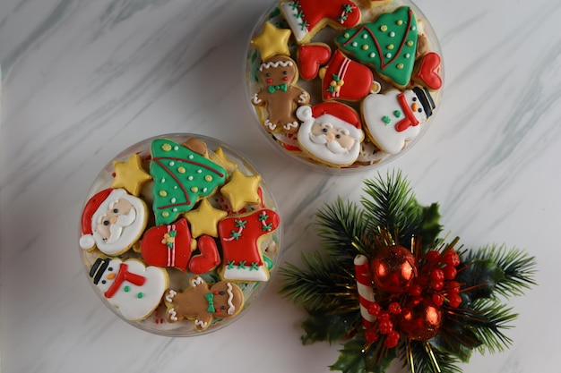 Biscoitos de natal decorados com glacê real na caixa plástica com fundo branco.