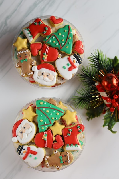 Biscoitos de natal decorados com glacê real na caixa plástica com fundo branco.