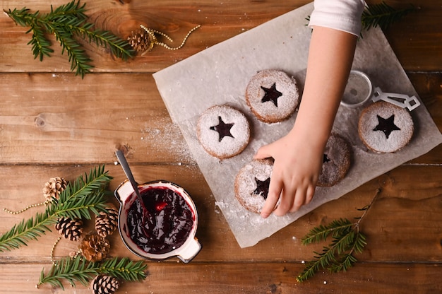 Biscoitos de Natal em forma de estrela em uma mesa de madeira. Biquitos com geléia e pó, decoração feita de ramos de abeto.