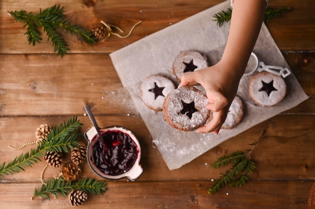 Biscoitos de Natal em forma de estrela em uma mesa de madeira. Biquitos com geléia e pó, decoração feita de ramos de abeto.