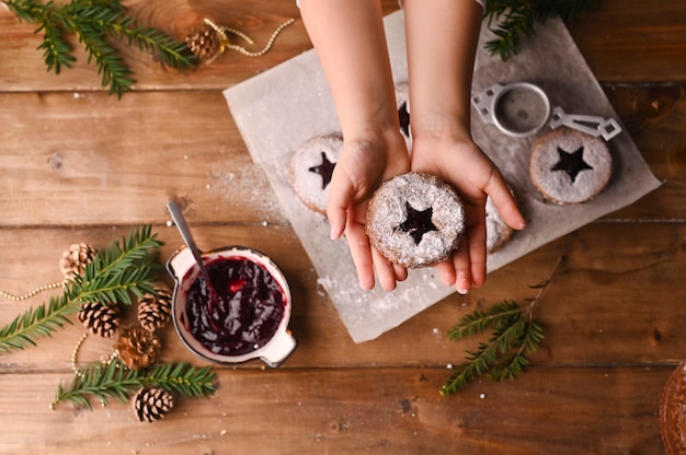 Biscoitos de Natal em forma de estrela em uma mesa de madeira. Biquitos com geléia e pó, decoração feita de ramos de abeto.