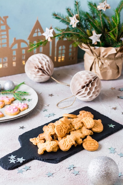 Biscoitos de Natal recém-assados são empilhados em uma lousa sobre uma mesa decorada. Deleite festivo. Visão vertical