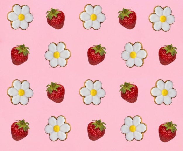 Biscoitos de pão de gengibre em forma de camomila e morango no fundo rosa Vista superior