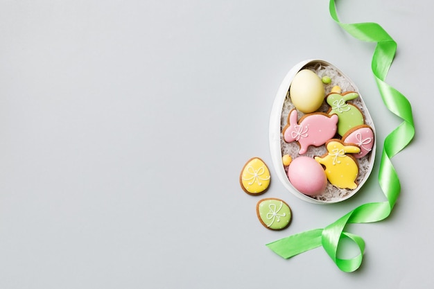 Biscoitos de páscoa coloridos na cesta com ovos de páscoa multicoloridos em fundo colorido Conceito de férias de ovos de páscoa de cor pastel com espaço de cópia