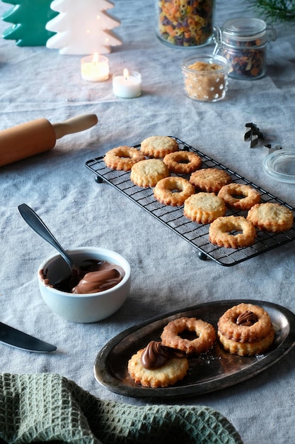 Biscoitos de sanduíche cheios de creme de nougat de avelã, velas de árvores de Natal na toalha de mesa de linho Luz natural