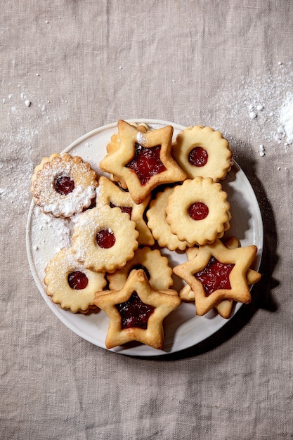 Biscoitos de shortbread linz tradicionais caseiros com geléia vermelha e açúcar de confeiteiro na placa de cerâmica sobre a toalha de mesa de linho. postura plana, espaço