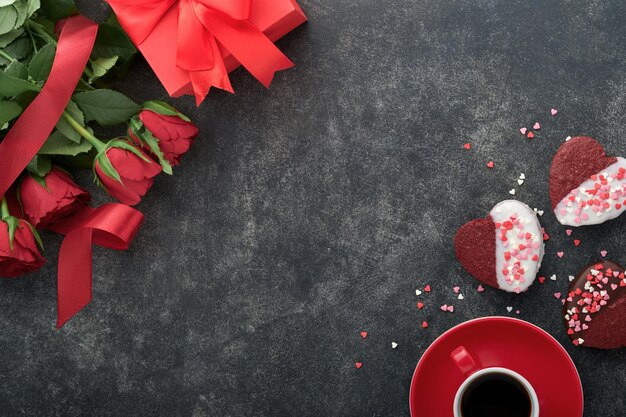 Biscoitos de veludo vermelho ou brownie em forma de coração em cobertura de chocolate com rosas vermelhas e caixa de presente em fundo preto Ideia de sobremesa para o Dia dos Namorados Mães ou Dia das Mulheres Sobremesa para o Dia dos Namorados