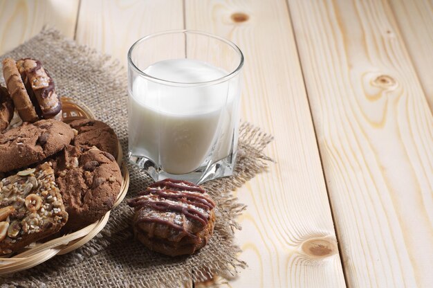 Biscoitos diferentes e um copo com leite no café da manhã em uma mesa de madeira
