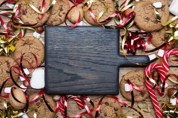 Biscoitos dos pedaços de chocolate Cenário vermelho e marshmallow do ouro do caramelo dos bastões do Natal em de madeira. Quadro de copyspace.