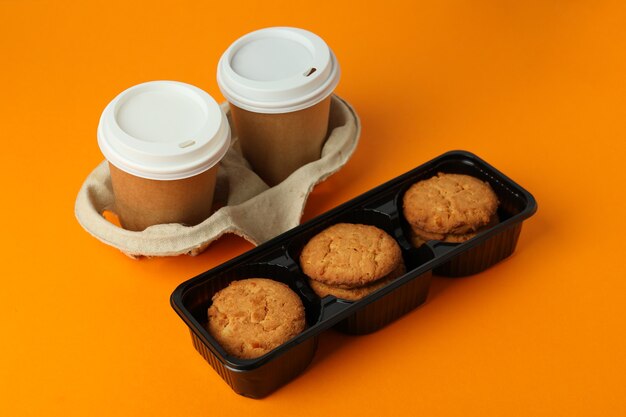 Biscoitos e copos de papel de café em fundo laranja.