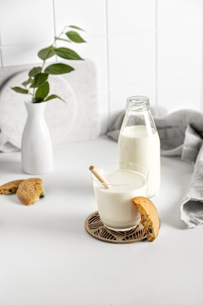 Biscoitos e leite em um copo e garrafa em uma mesa branca com um guardanapo e um pequeno vaso