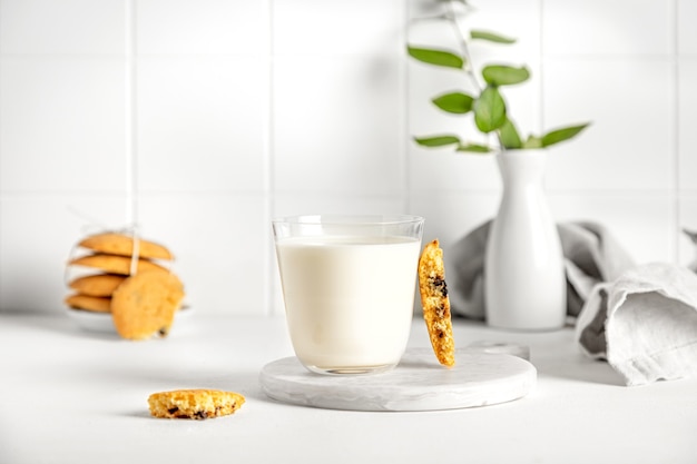 Biscoitos e leite em um copo sobre uma mesa branca com um guardanapo e um pequeno vaso