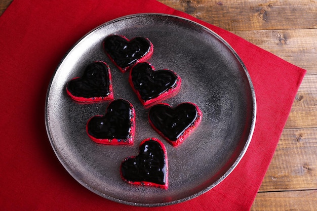 Biscoitos em forma de chocolate coberto de coração na bandeja de metal com guardanapo no fundo da mesa de madeira