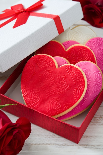 Biscoitos em forma de coração em caixa de presente decorada com rosas para dia dos namorados na mesa de madeira branca