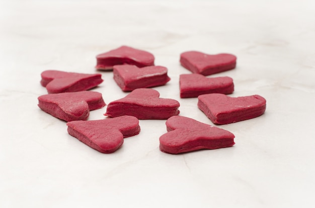 Biscoitos em forma de coração vermelhos em uma mesa branca closeup, assando no dia dos namorados