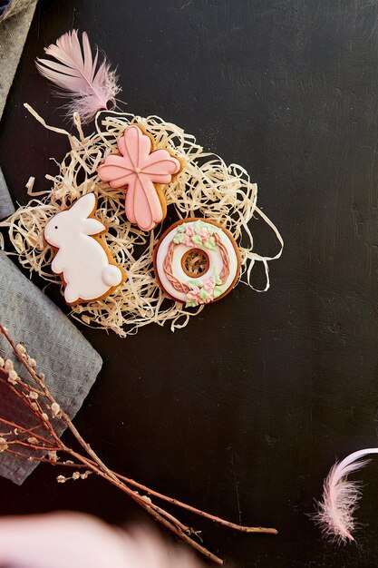 Biscoitos festivos da Páscoa decorados com penas e galhos de gatos da primavera em fundo preto, faixa plana da Páscoa