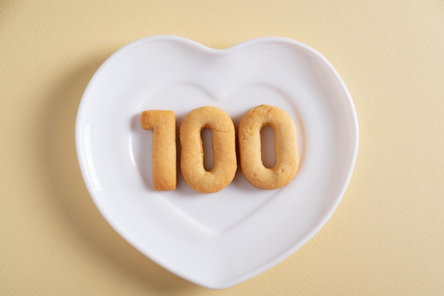 Biscoitos formando o número 100 na placa branca e fundo amarelo claro