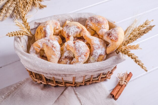 Biscoitos frescos e saborosos com canela em uma cesta de vime em um fundo branco de madeira