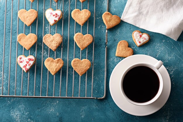 Biscoitos gelados caseiros em forma de coração na grelha de metal com uma xícara de chá vermelho