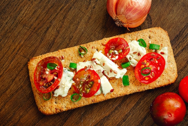 Biscoitos integrais pão torrado fino com queijo tomate cebola e sementes de linho em fundo de madeira natural