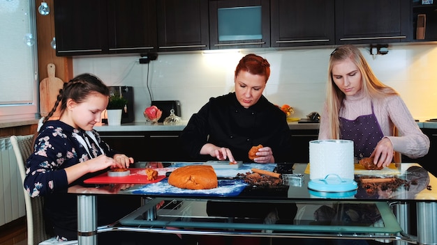 Biscoitos masterclass fazendo em uma atmosfera alegre em casa duas mulheres e uma menina recheando uma assadeira com ...