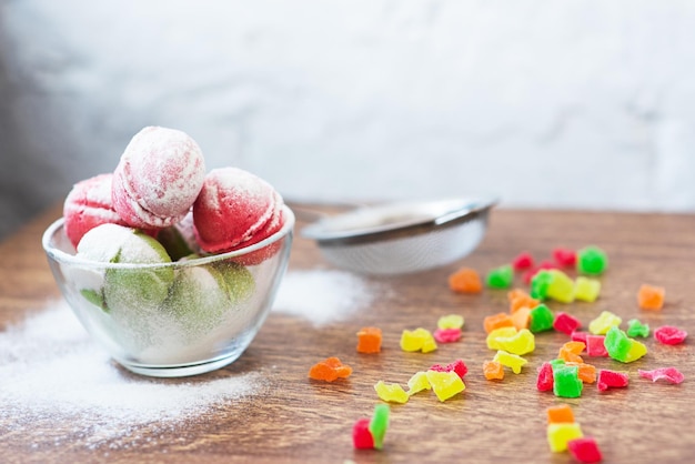 Biscoitos multicoloridos em forma de nozes com creme recheado e frutas cristalizadas e xícara de café em uma mesa de madeira biscoitos caseiros espaço para cópia doces saborosos