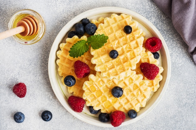 Biscoitos ondulados waffle com framboesas frescas e mirtilos em uma mesa de concreto. Copie o espaço.