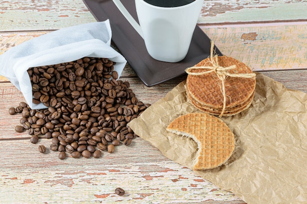 Biscoitos stroopwafel com uma mordida ao lado de feijão e xícara de café.