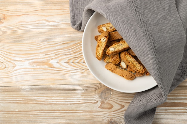 Biscotti di prato sobre fondo de arpillera mantel rústico. Galletas de nueces cantuccini italianas tradicionales. Galletas de mantequilla cantucci caseras con almendras en la vista superior de la placa blanca